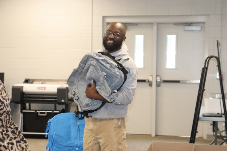 Coach Dee smiles with a backpack