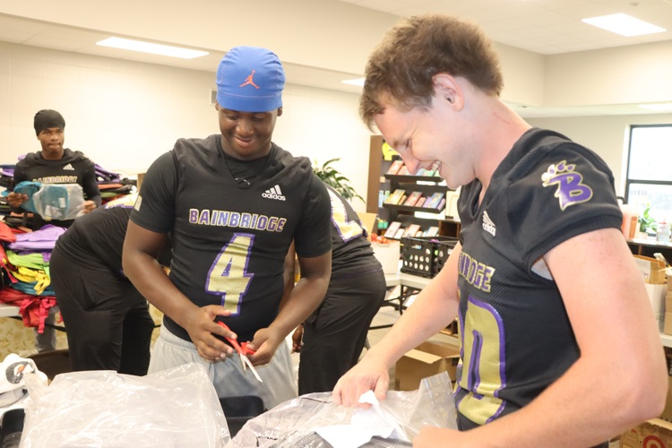 2 BHS football players put schools supplies in a backpack