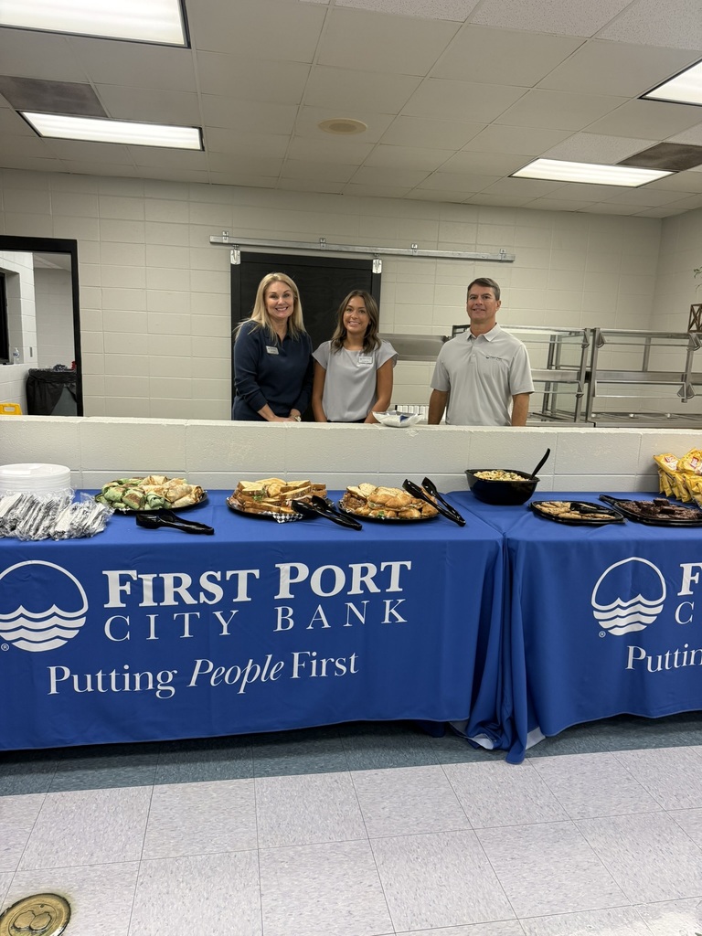 Three First Port City Bank representatives stand behind a catered lunch featuring sandwiches, wraps, chips, and desserts for new Decatur County Schools teachers.
