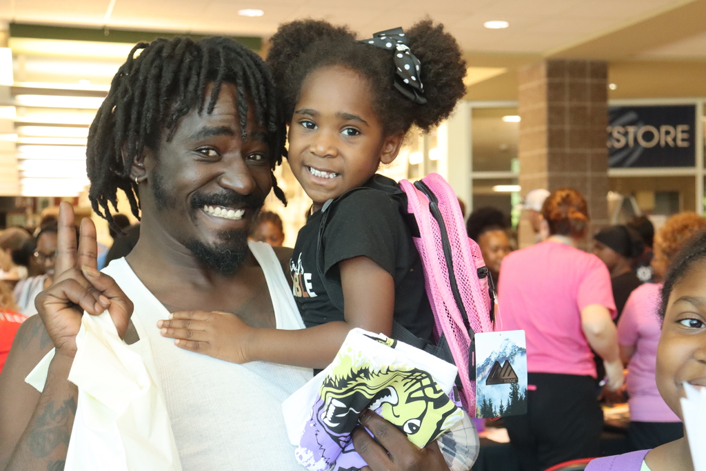 A smiling father holds his daughter, who is wearing a new pink backpack, at Bearcat Blitz.