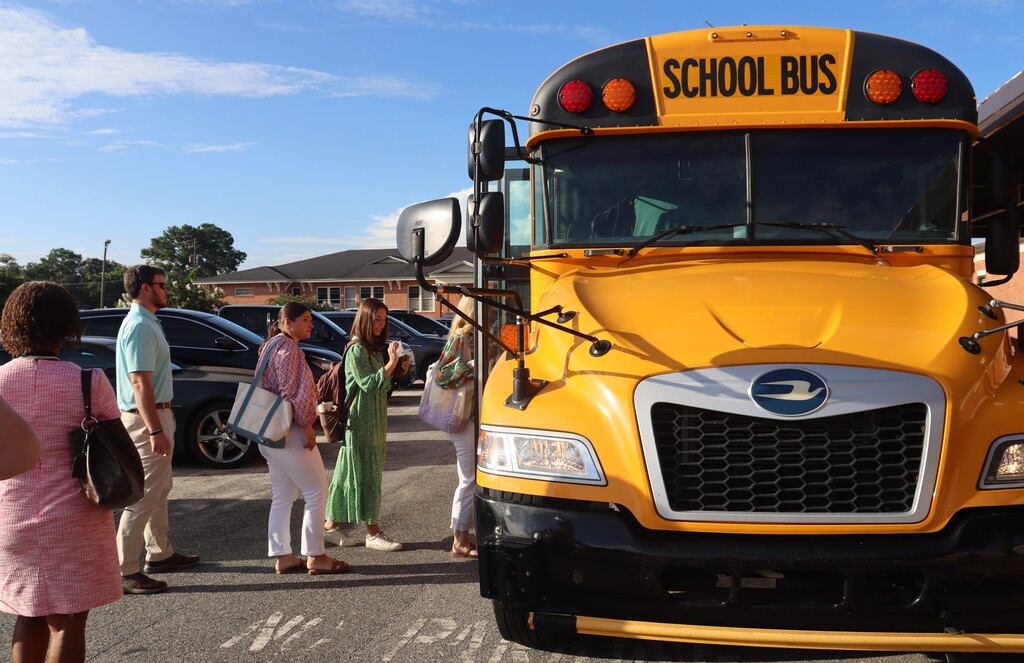 New teachers gather beside a school bus for a district tour.