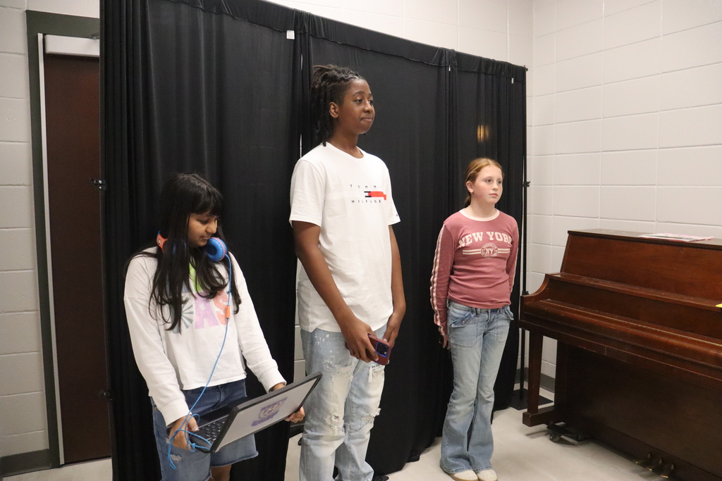 Three Bainbridge Middle School students stand in front of a black curtain during fall play auditions, with one student holding a laptop.