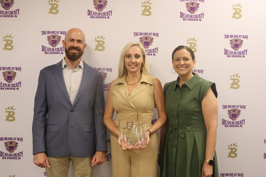 Candance Rentz stands receiving award alongside Sean Johnson and Christy Cox with a Decatur County Schools Bearcat Branded Media backdrop in the background