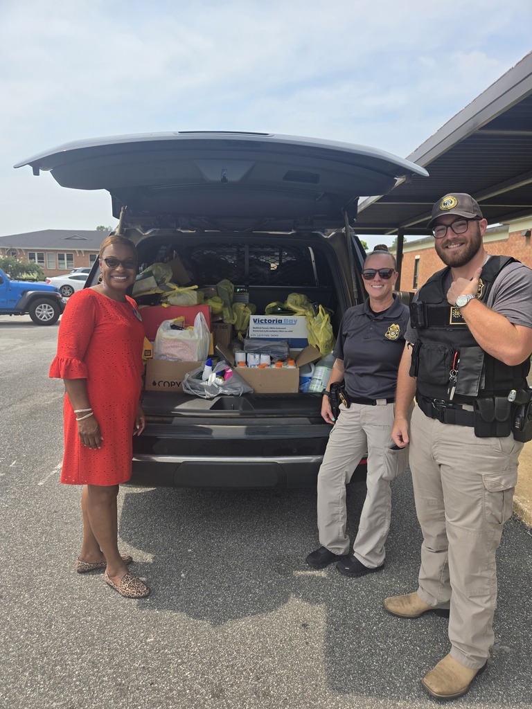 Three people stand beside a vehicle filled with donated school supplies.