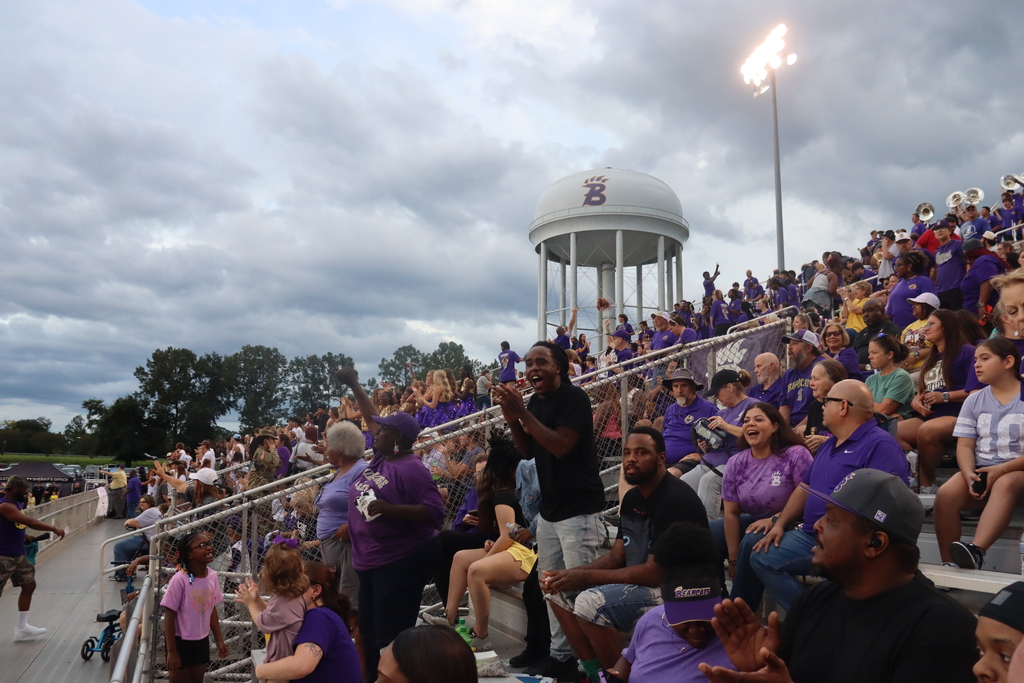 Bearcat fans cheer from the stadium stands with the water tower in the background.