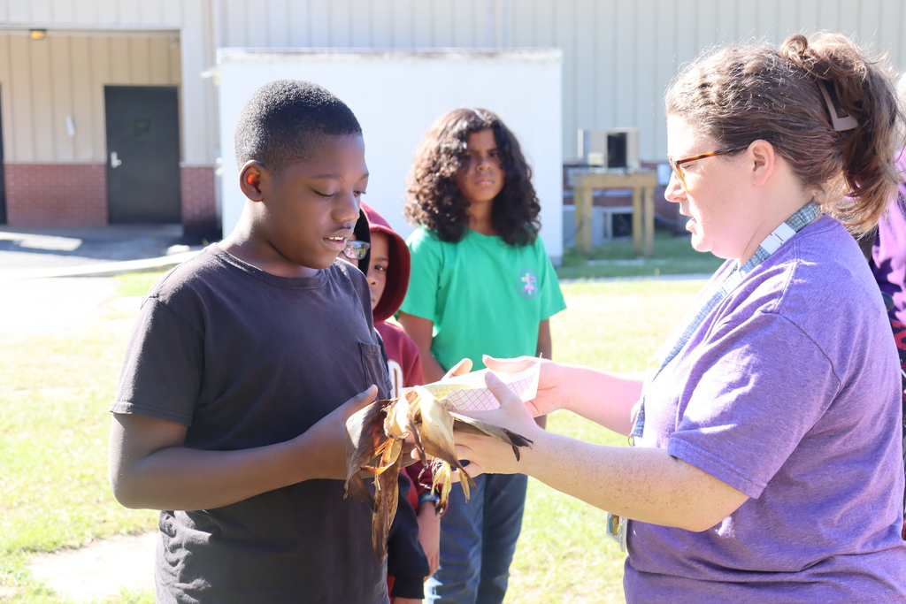 child receiving a piece of roasted corn from teacher and smiling
