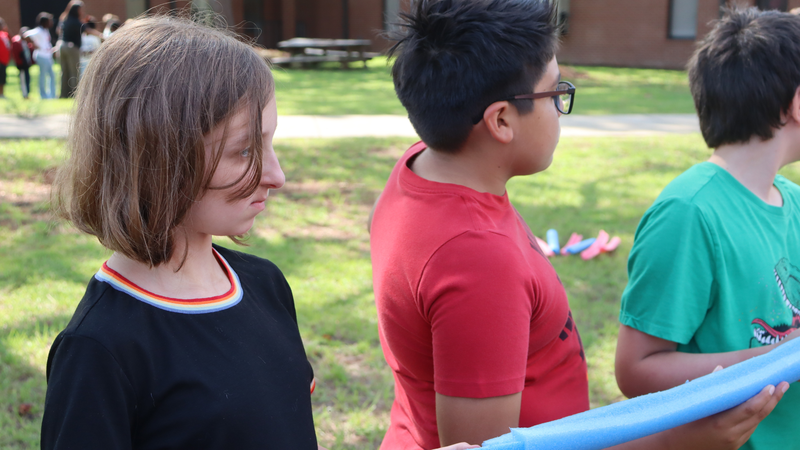 Students work together with a foam tube during an outdoor STEM challenge.