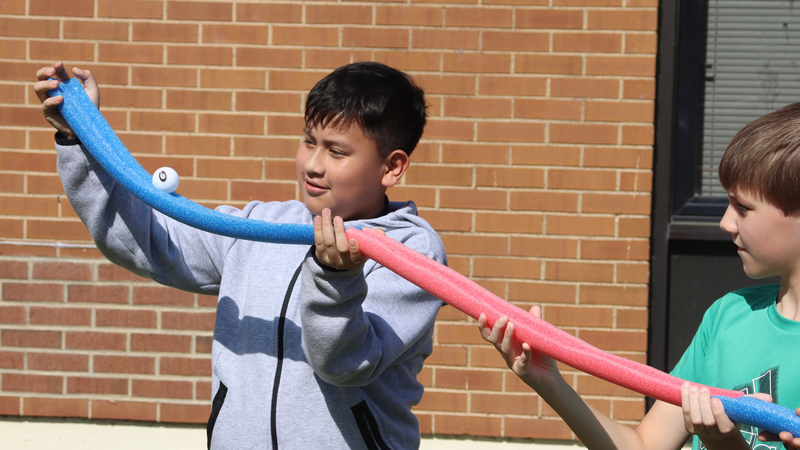 Students work together with a foam tube during an outdoor STEM challenge.