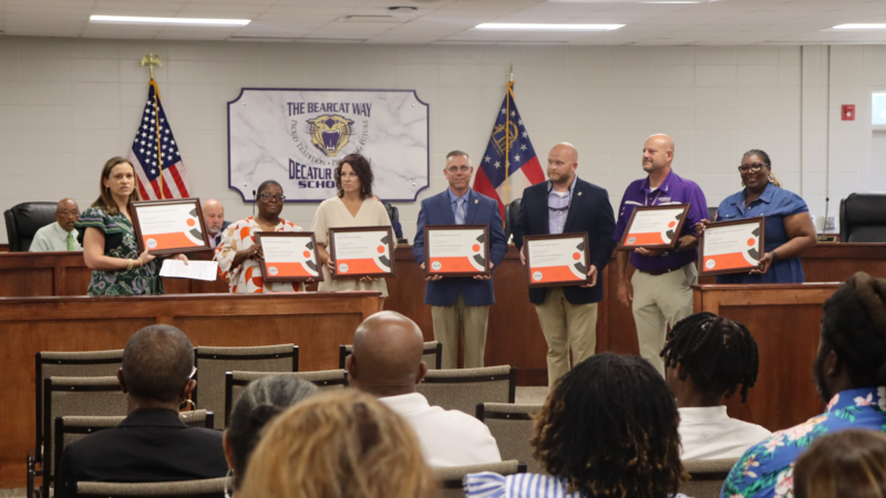 Decatur County Schools representatives holding Cognia accreditation certificates during a board meeting, with audience members seated in the foreground.