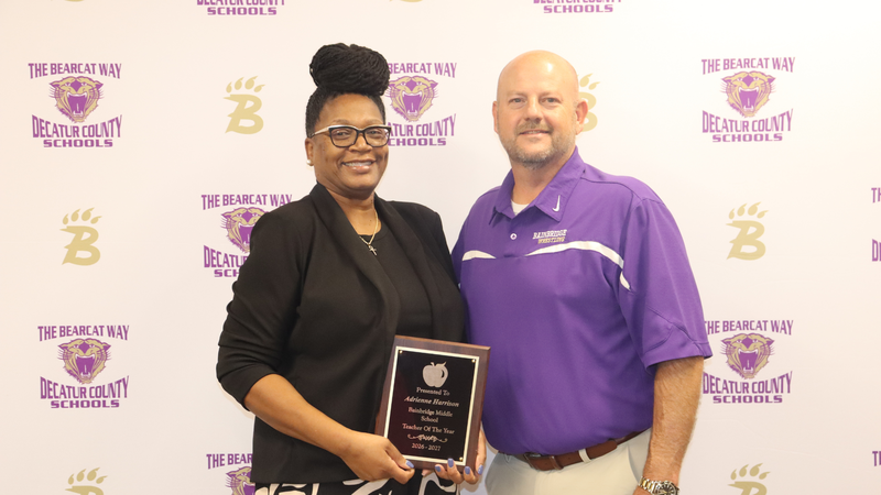Teacher and principal stand holding award in front of a branded decatur county schools media backdrop