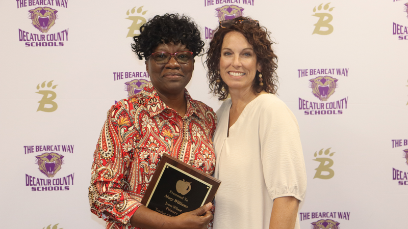 Teacher and principal stand holding award in front of a branded decatur county schools media backdrop