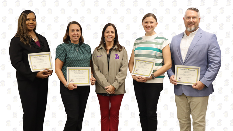 Five individuals stand in front of a Decatur County Schools backdrop, with four holding certificates of achievement.