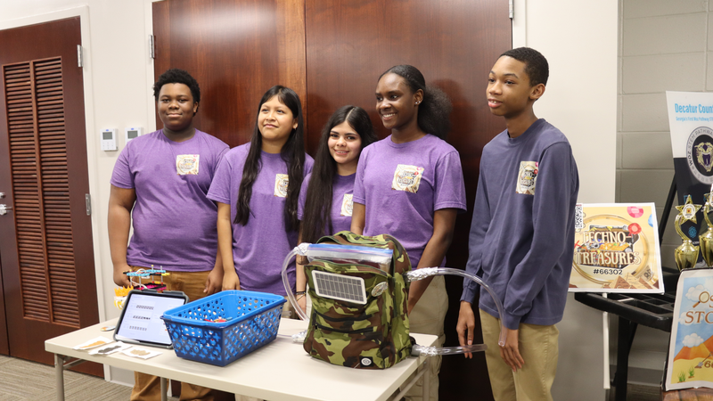 BMS robotics students stand with their innovation project display and prototype.