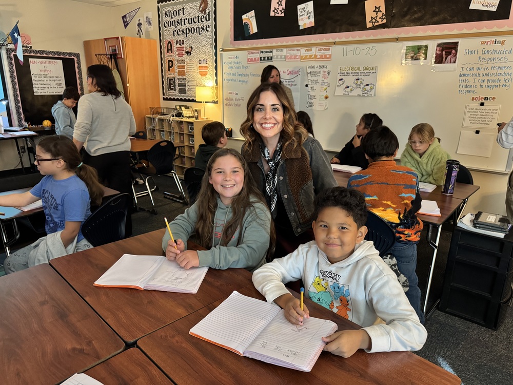 Taylor Williams and two students smile for the camera inside a classroom