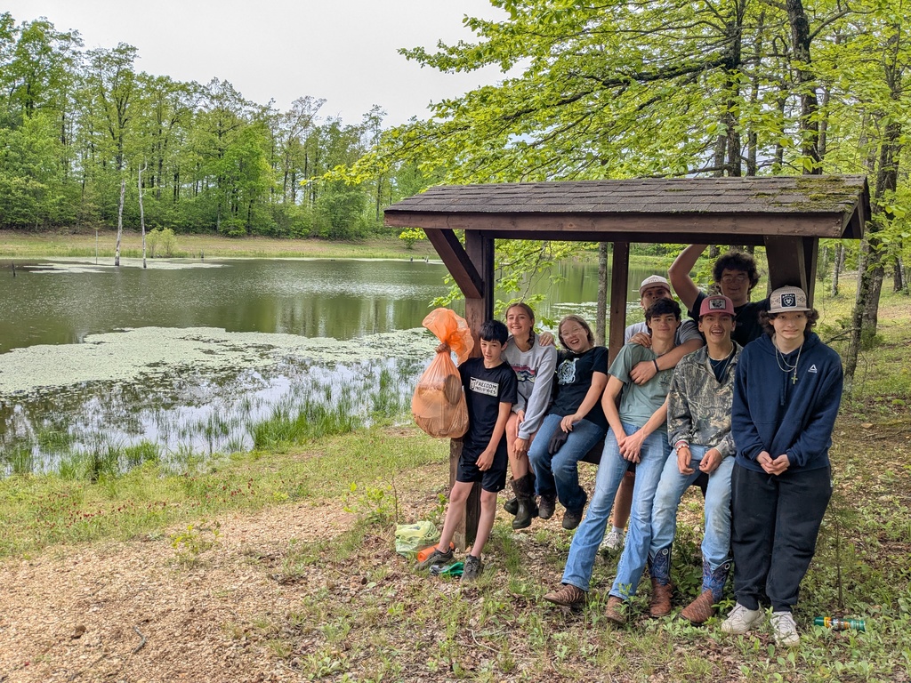 students with a trash bag full of litter with a pond in the background