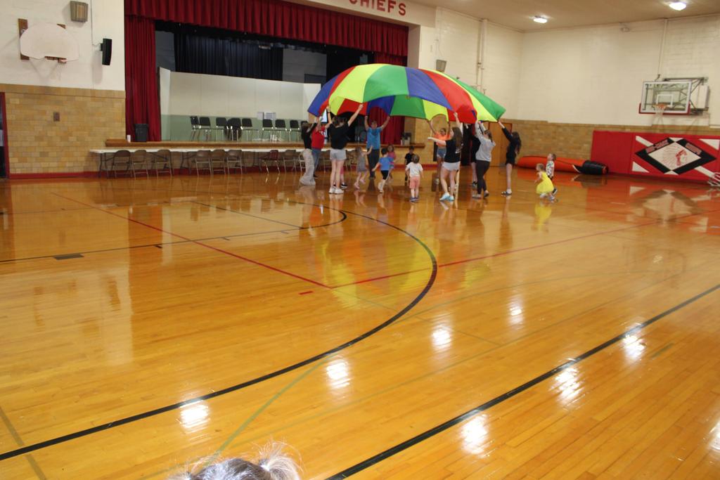 High school and preschool studnets playing with a parachute in the gym
