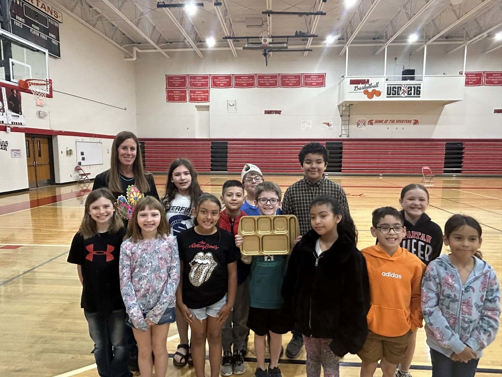 4th grade students standing in gym with golden lunch tray award