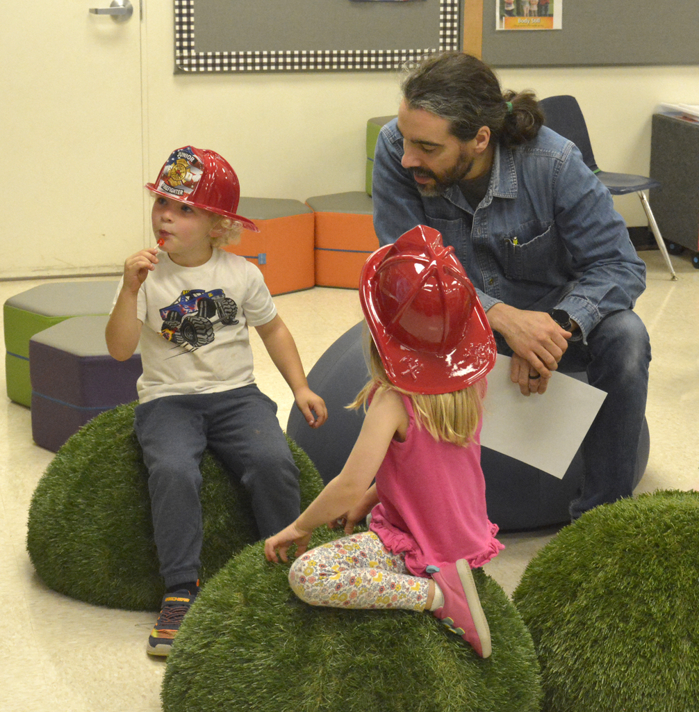 adult speaks with two children wearing fire helmets