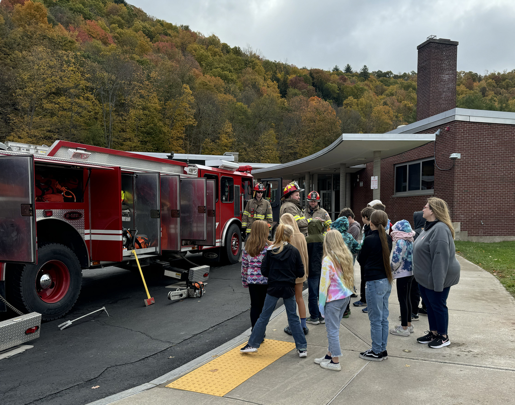 firefighters speak with children in front of a fire truck