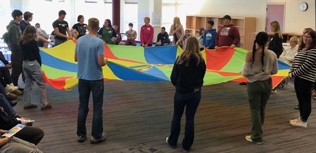 students and adult advisors hold a colorful parachute