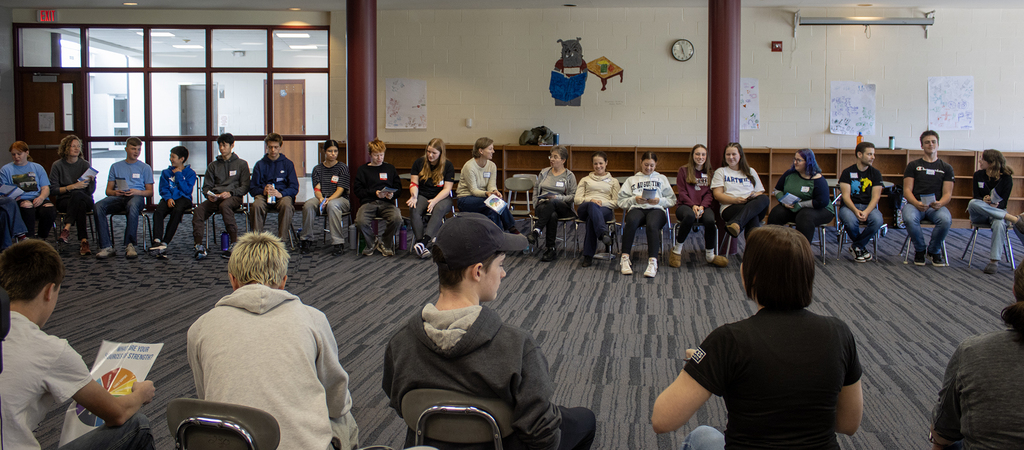 students and adult advisors sit in a circle of chairs