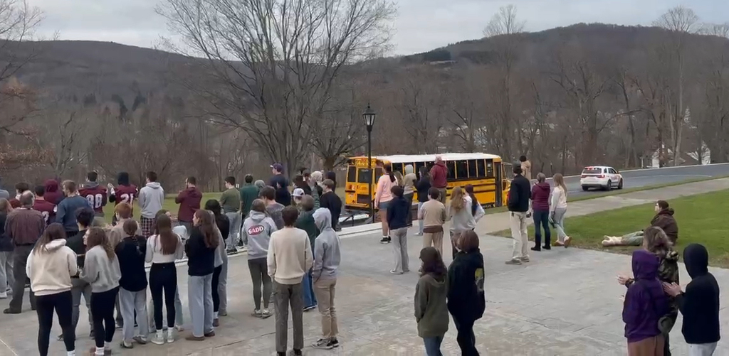students gather in front of school to cheer on bus
