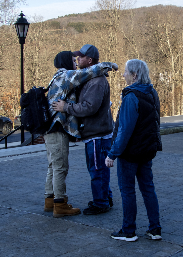 a boy hugs his dad as his grandmother watches