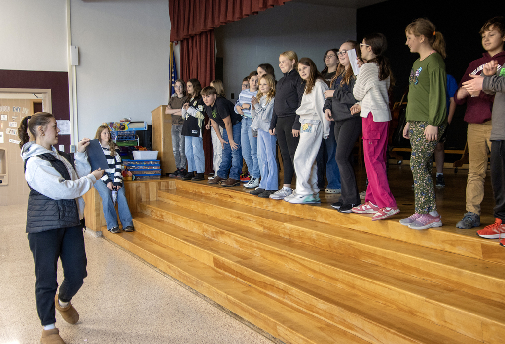 elementary students on stage, 2 high schoolers working with them