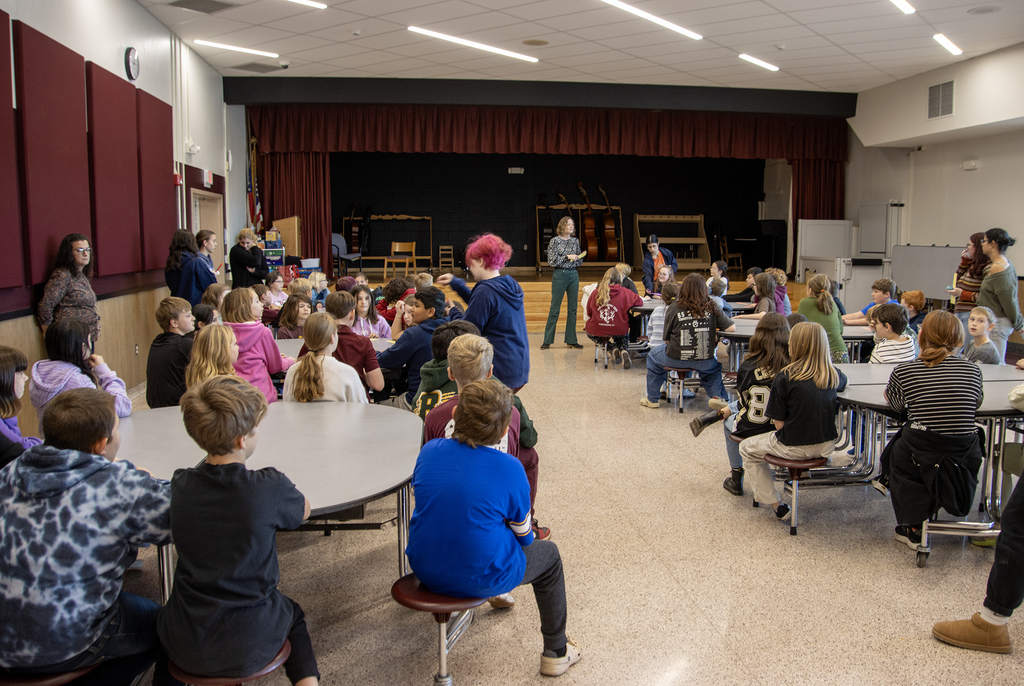 adult speaks to room with elementary students and high school peer counselors