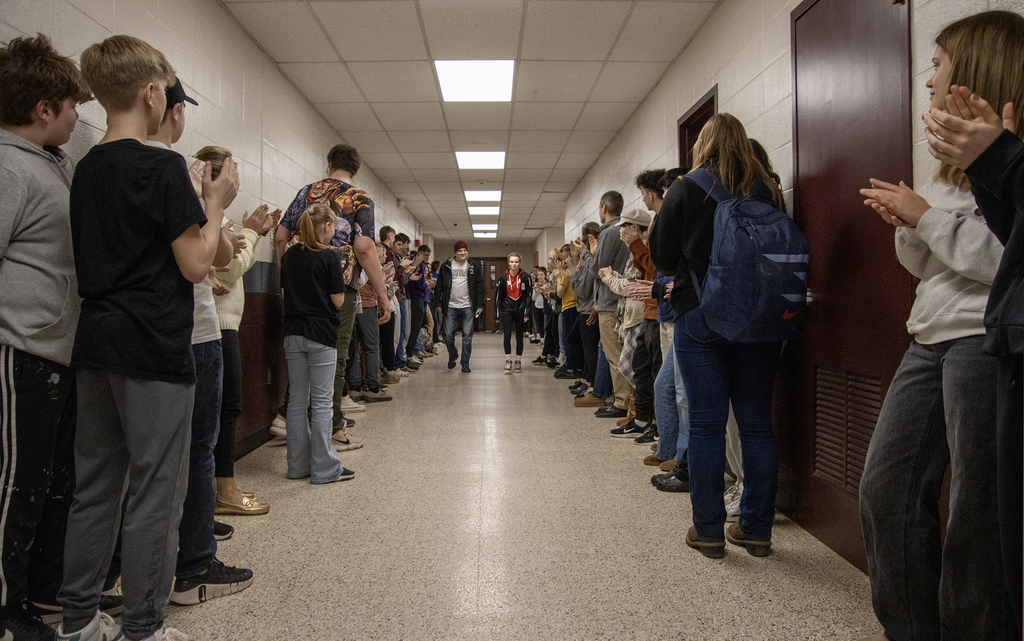 coach and Cadence Guy walk down a hall of cheering students and staff