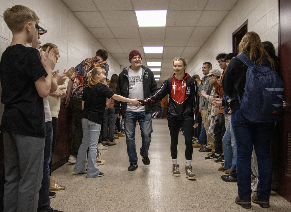 coach and Cadence Guy walk down a hall of cheering students and staff