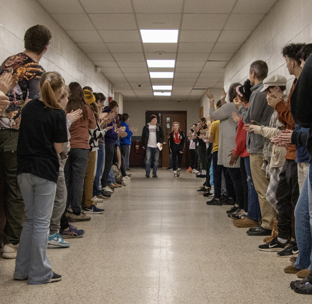 coach and Cadence Guy walk down a hall of cheering students and staff