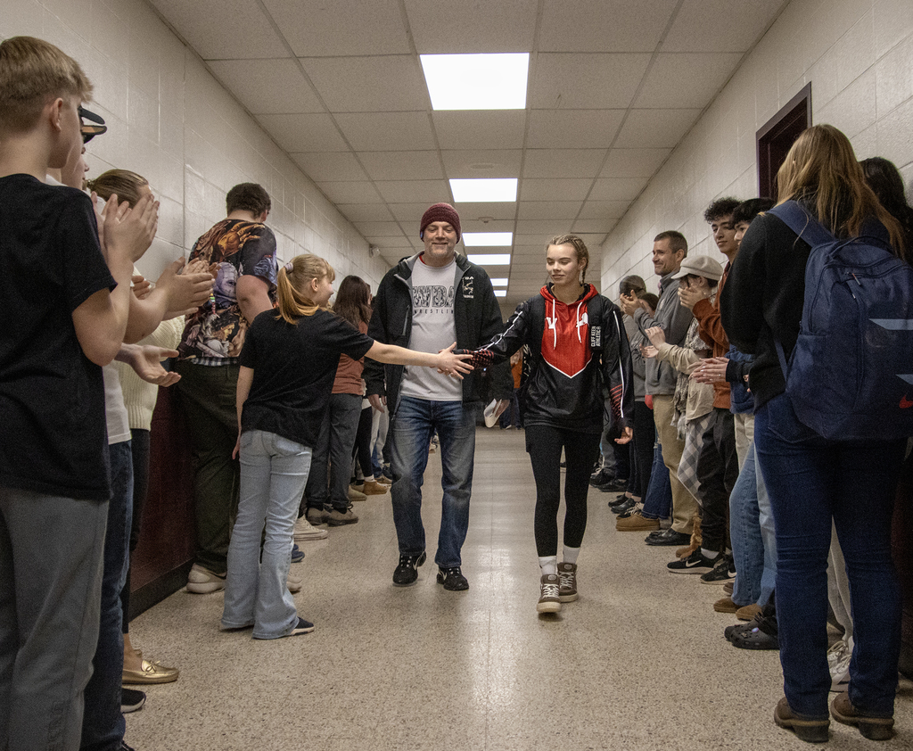 coach and Cadence Guy walk down a hall of cheering students and staff, Cadence high fives a sudent