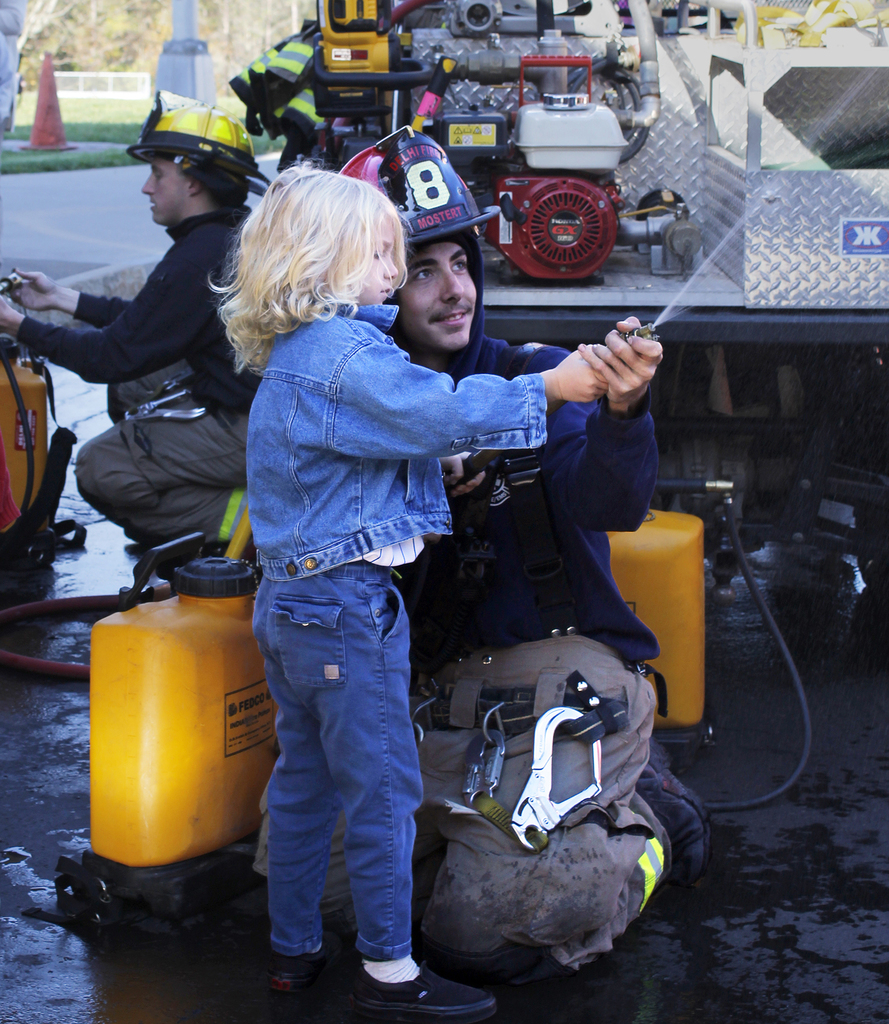 child with firefighter, spraying from hose