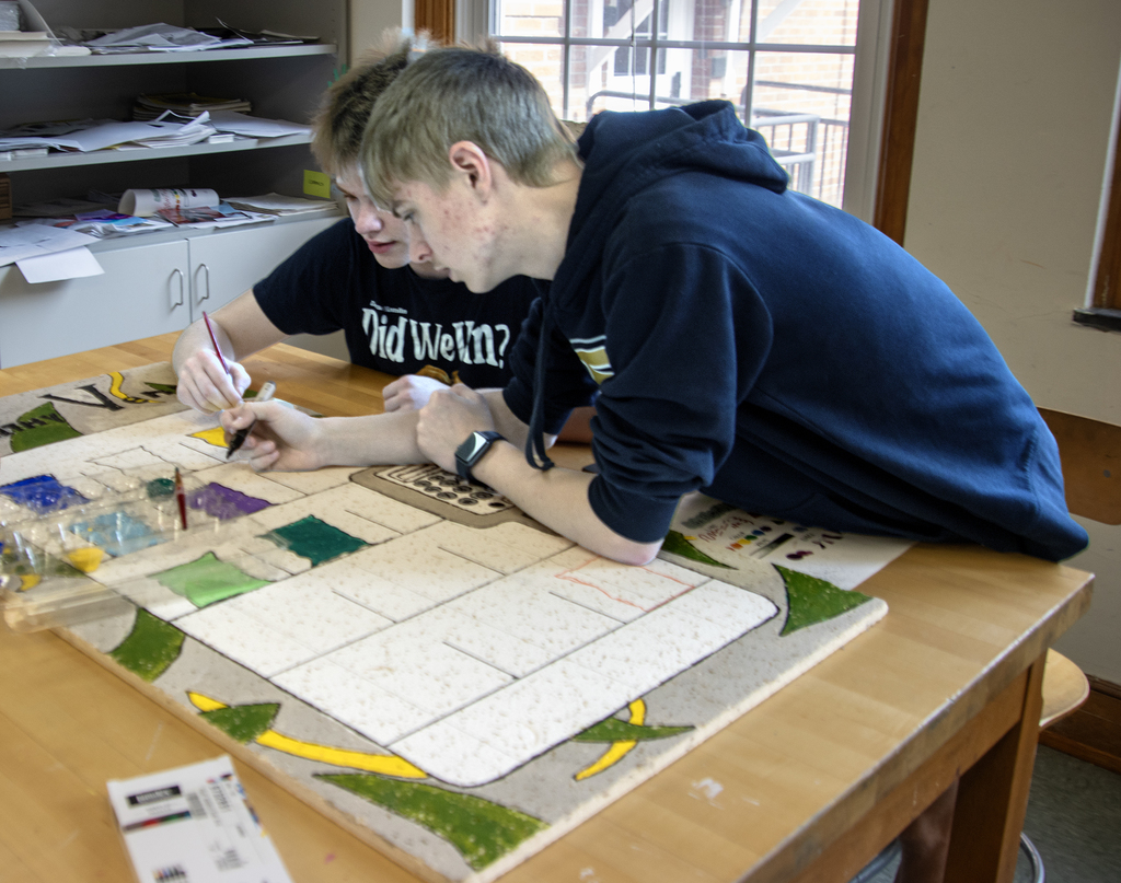 2 students wqork on painting a ceiling tile