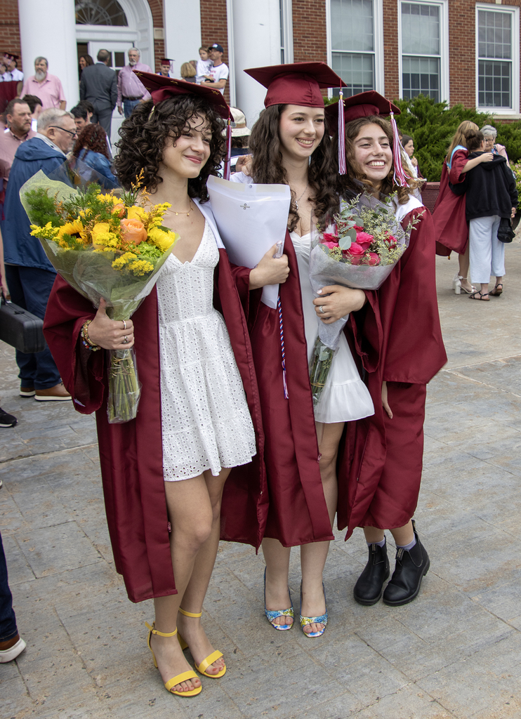 3 graduates pose for pictures in front of school