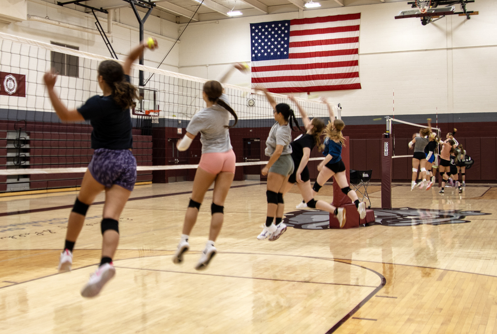 volleyball players leap into air at net