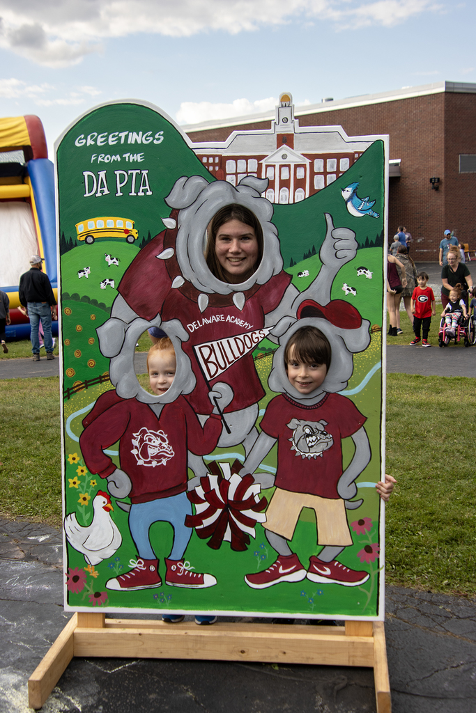 adult and two children pose in photo cutout that says Greetings from DA PTA!