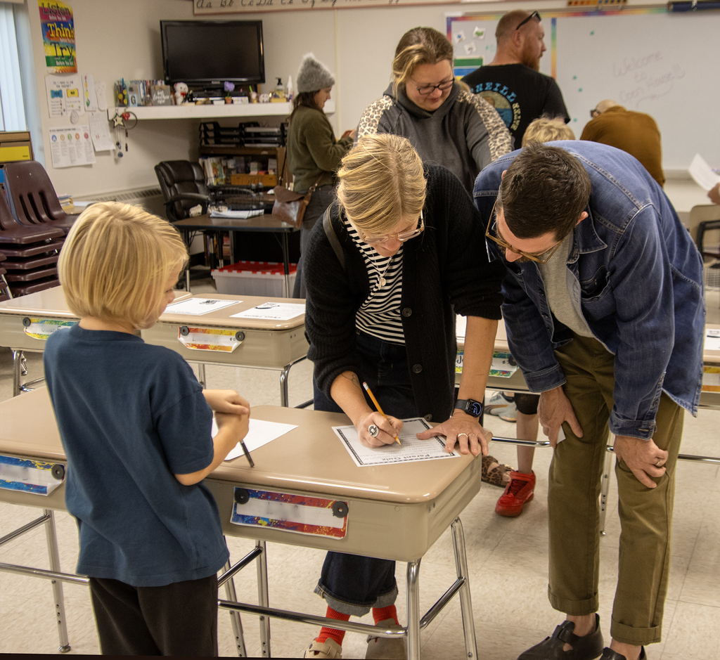 family looking at work with student, teacher in background