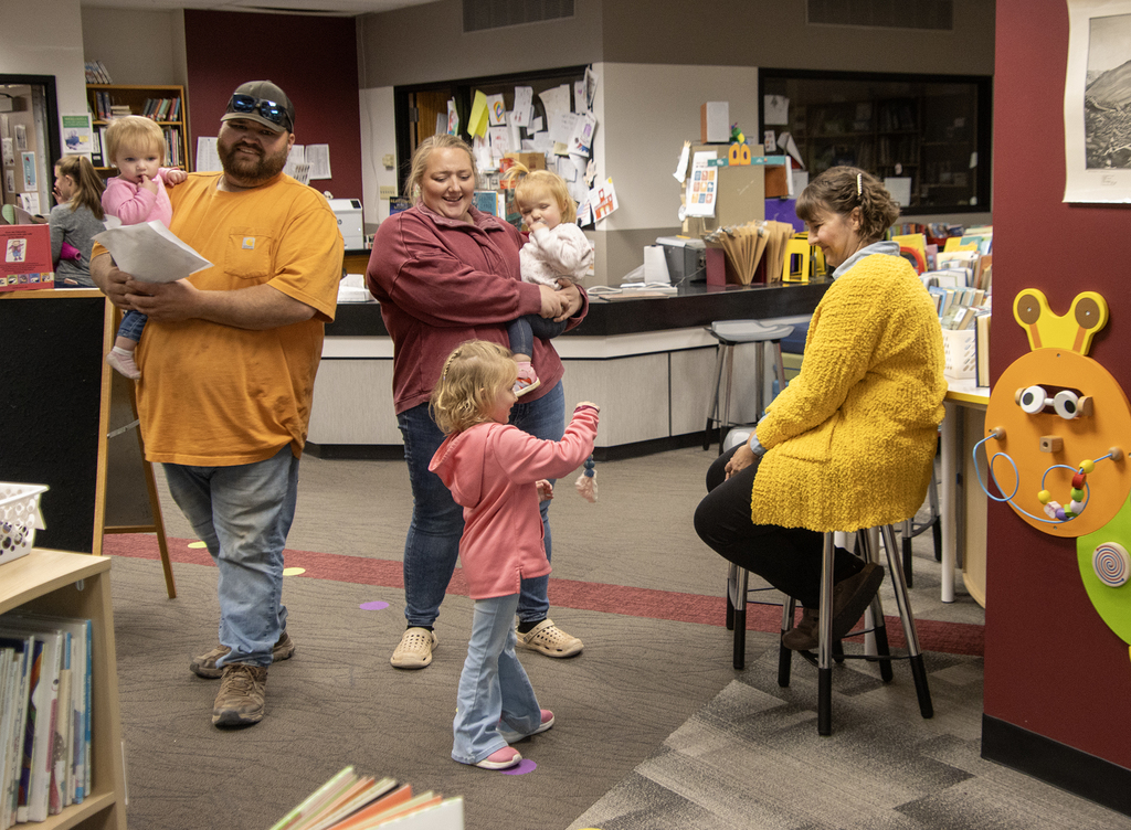 child shows something to librarian while family watches