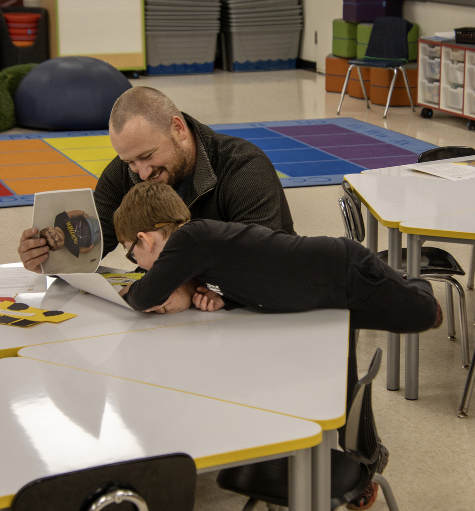 father smiles as son lays on table and points to papers