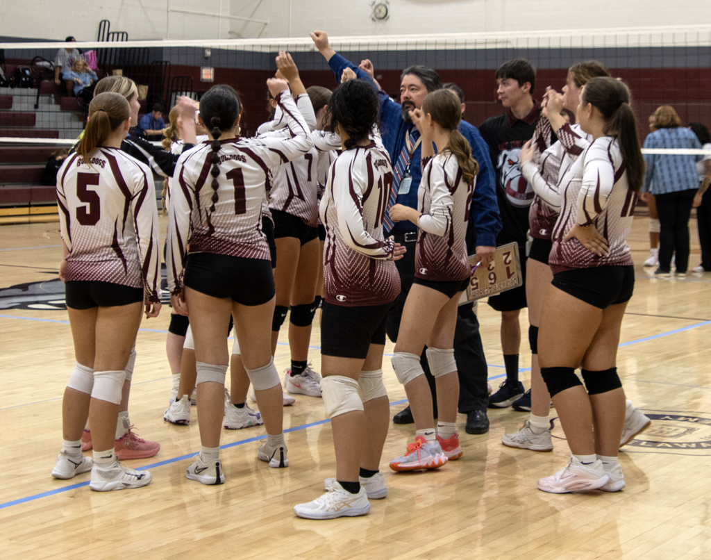 Volleyball team and coach gathered for a huddle at net