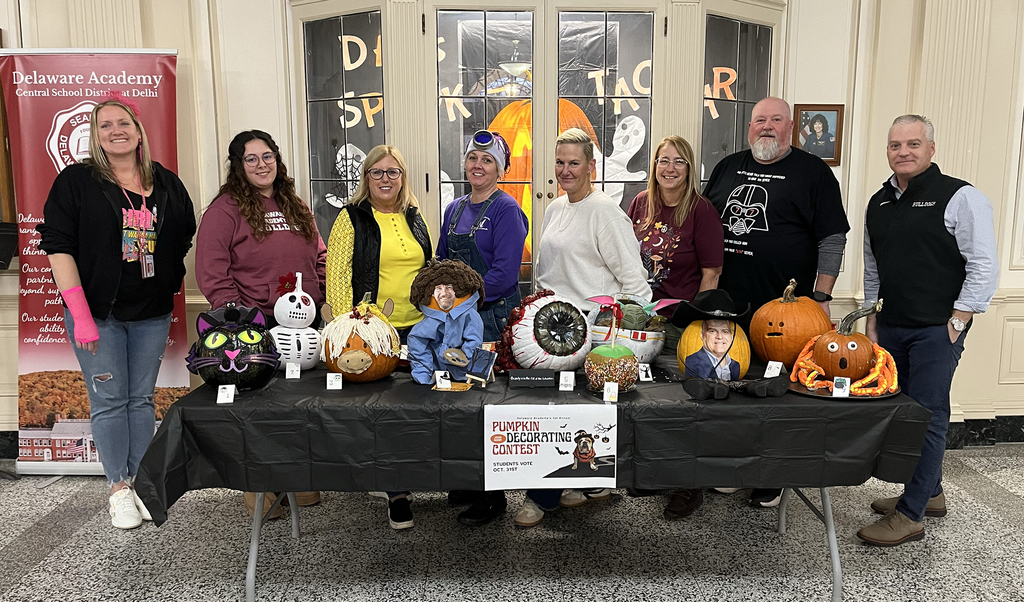 8 adults stand behind table full of decorated pumpkins