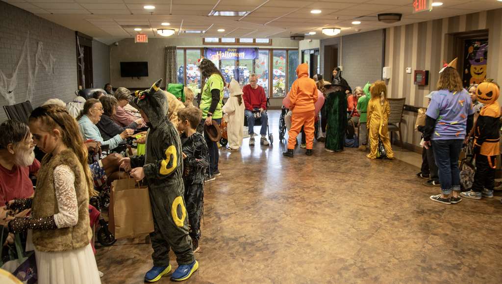 2nd grade students in costume visit with residents of nursing home, who hand out candy