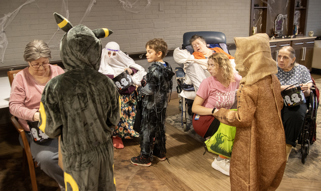 2nd grade students in costume visit with residents of nursing home, who hand out candy