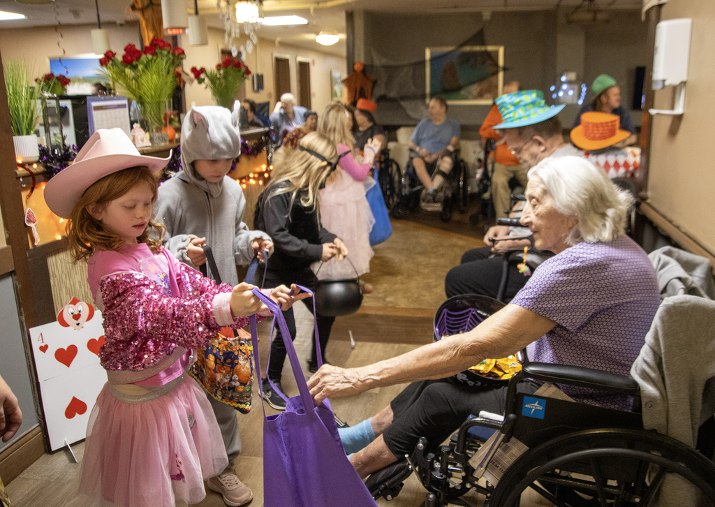 2nd grade students in costume visit with residents of nursing home, who hand out candy