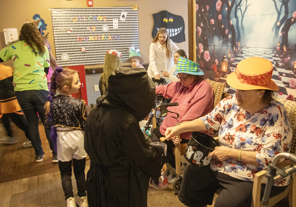 2nd grade students in costume visit with residents of nursing home, who hand out candy