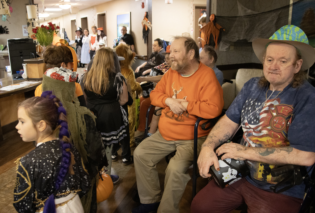 2nd grade students in costume visit with residents of nursing home, who hand out candy