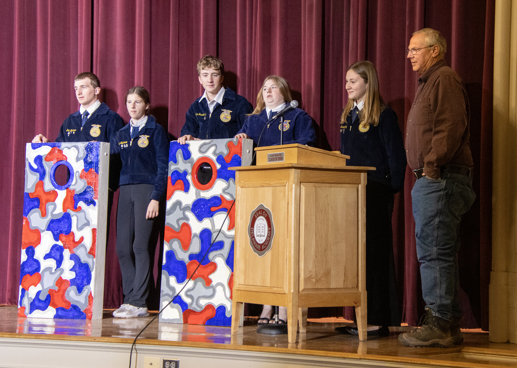 5 FFA members pose with a veteran and cornhole boards