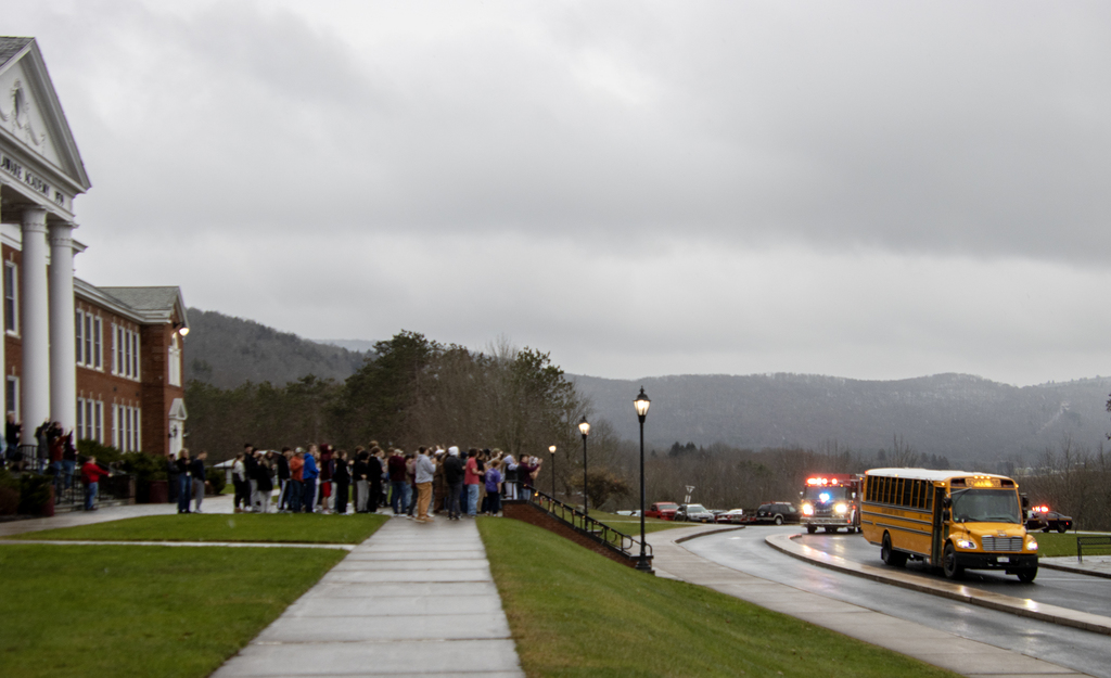 students gather in front of school to cheer on bus and emergency vehicles